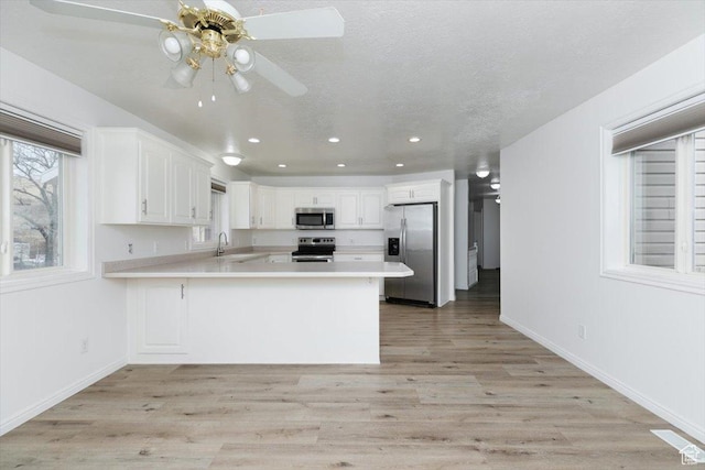 kitchen featuring sink, light hardwood / wood-style flooring, kitchen peninsula, stainless steel appliances, and white cabinets