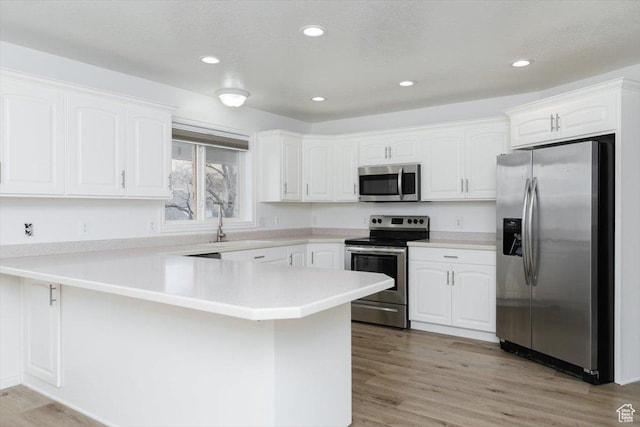 kitchen with a textured ceiling, light hardwood / wood-style flooring, appliances with stainless steel finishes, kitchen peninsula, and white cabinets