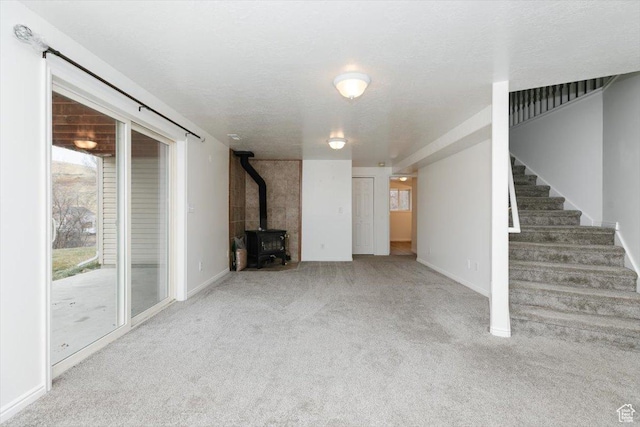 unfurnished living room featuring a wood stove, light carpet, and a textured ceiling