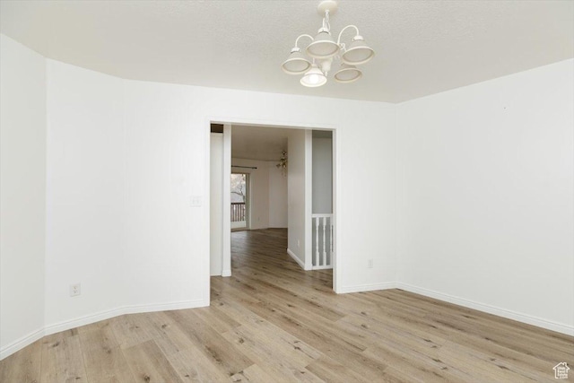 unfurnished room featuring a textured ceiling, an inviting chandelier, and light hardwood / wood-style flooring