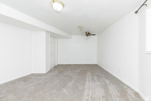 basement featuring ceiling fan, light carpet, and a textured ceiling