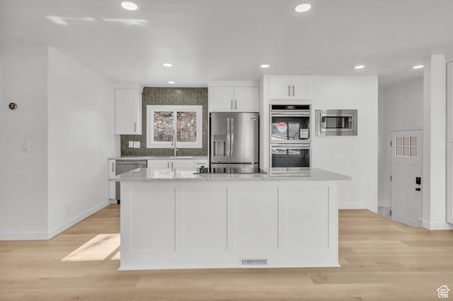 kitchen with a kitchen island, white cabinetry, sink, light stone counters, and stainless steel appliances