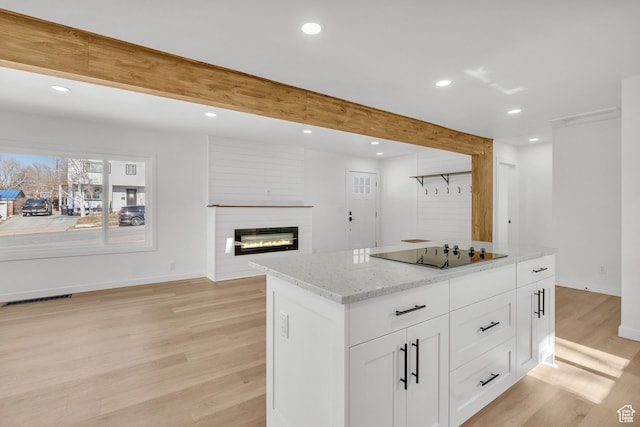 kitchen with beamed ceiling, white cabinets, black electric stovetop, light stone counters, and light wood-type flooring