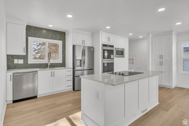 kitchen featuring sink, white cabinetry, light stone counters, a kitchen island, and stainless steel appliances