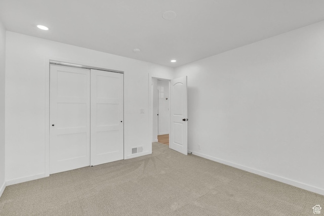 unfurnished bedroom with light colored carpet and a closet