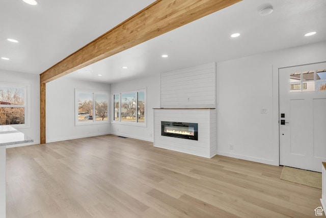 unfurnished living room with beamed ceiling, a large fireplace, and light hardwood / wood-style floors
