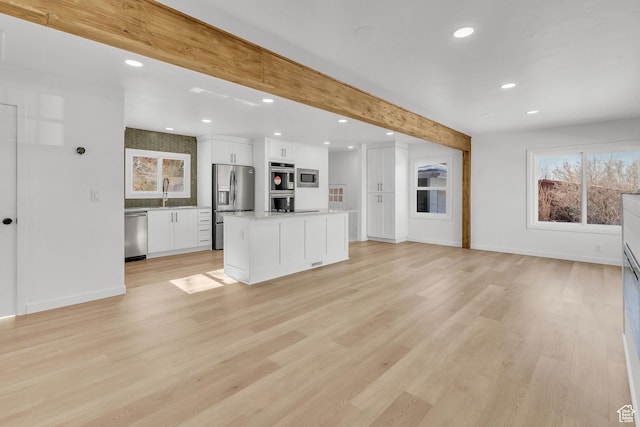 unfurnished living room with beamed ceiling, sink, and light hardwood / wood-style floors