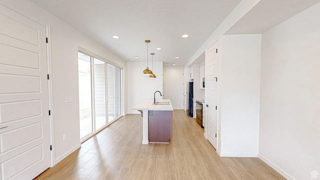 kitchen featuring sink, decorative light fixtures, refrigerator, light hardwood / wood-style flooring, and a kitchen island with sink