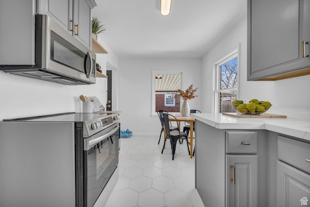 kitchen featuring gray cabinetry, baseboards, light tile patterned flooring, and appliances with stainless steel finishes