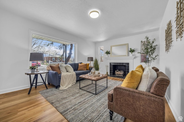 living area featuring a tile fireplace, baseboards, and wood finished floors
