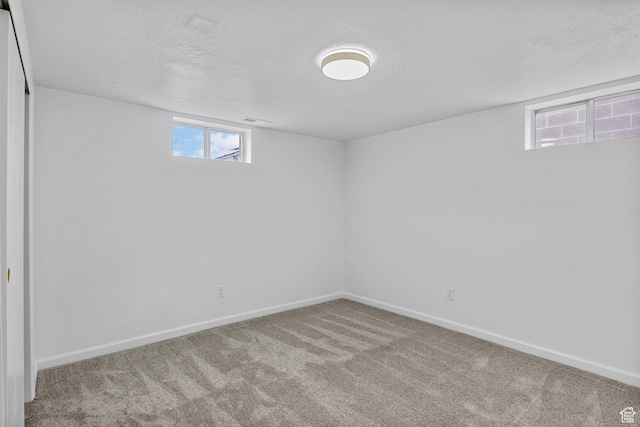 below grade area with a textured ceiling, baseboards, visible vents, and carpet floors