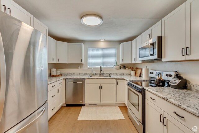 kitchen with appliances with stainless steel finishes, sink, white cabinets, light stone counters, and light wood-type flooring