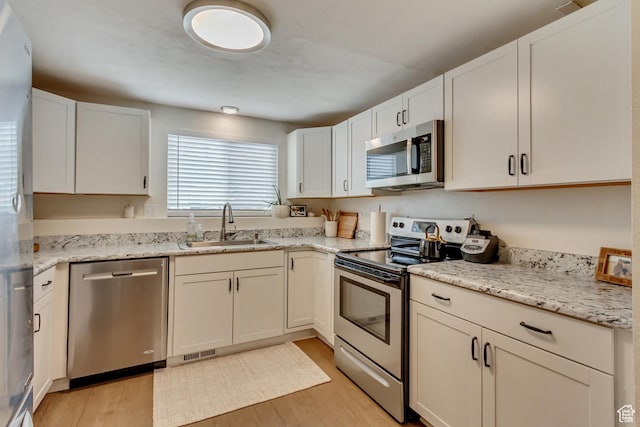 kitchen with sink, white cabinetry, light stone counters, light wood-type flooring, and appliances with stainless steel finishes