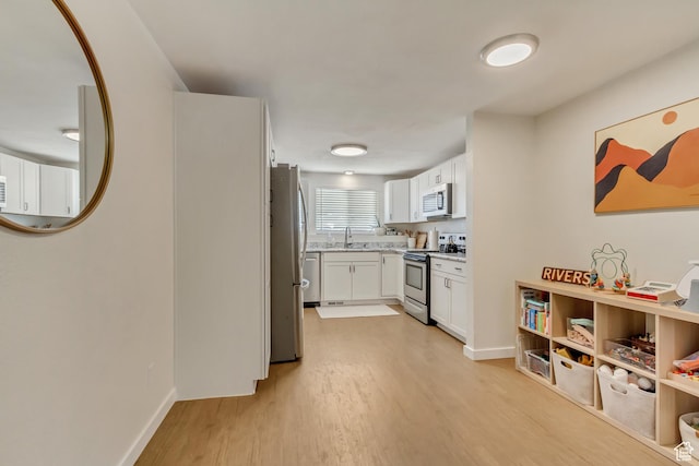 kitchen with appliances with stainless steel finishes, sink, white cabinets, and light hardwood / wood-style floors