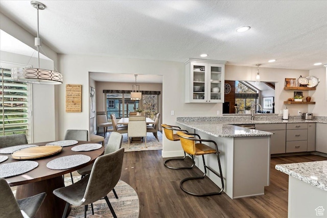 kitchen with pendant lighting, a breakfast bar, light stone counters, white cabinets, and kitchen peninsula