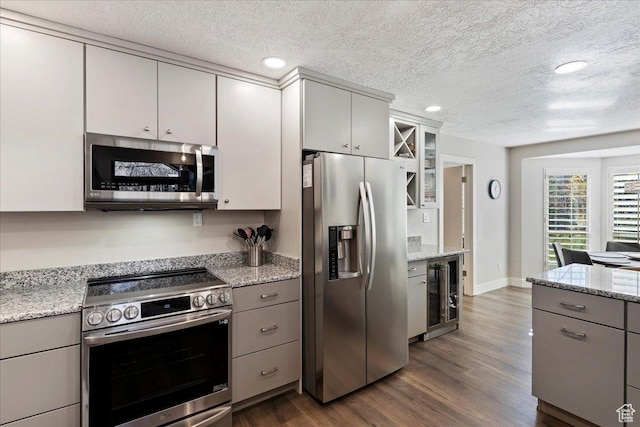 kitchen featuring light stone countertops, dark hardwood / wood-style floors, stainless steel appliances, and beverage cooler
