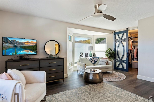 living area featuring ceiling fan, a barn door, dark hardwood / wood-style flooring, and a textured ceiling