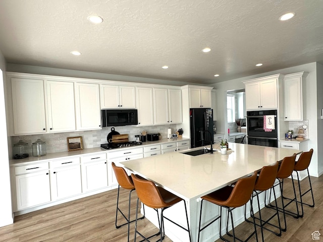 kitchen featuring sink, white cabinetry, a kitchen bar, black appliances, and a center island with sink