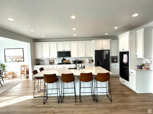 kitchen with white cabinetry, a kitchen island with sink, a kitchen bar, and black appliances