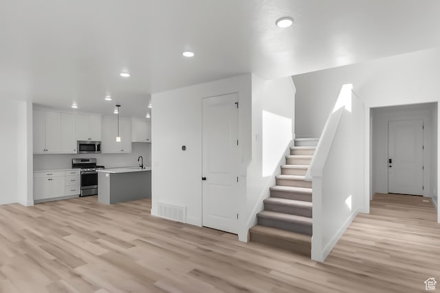 3463 W 3175 N Unit 362, Plain City, UT 84404 - kitchen featuring decorative light fixtures, light hardwood / wood-style flooring, stainless steel appliances, a kitchen island with sink, and white cabinets