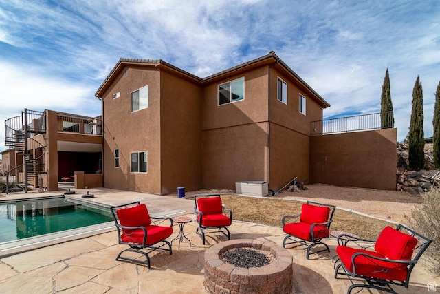 rear view of property featuring stairway, an outdoor fire pit, a patio, an outdoor pool, and stucco siding