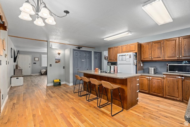 kitchen featuring brown cabinetry, freestanding refrigerator, a kitchen island, a kitchen bar, and stainless steel microwave