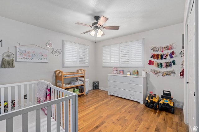 bedroom featuring baseboards, light wood-style flooring, a crib, and a ceiling fan