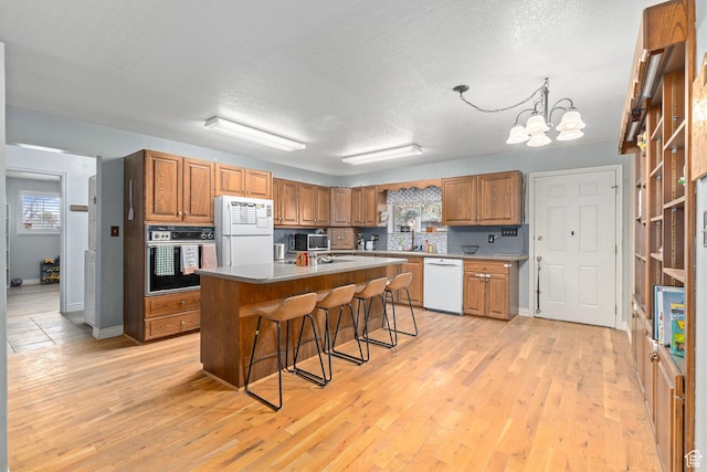 kitchen with an inviting chandelier, white appliances, a breakfast bar area, brown cabinets, and light wood finished floors