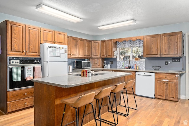 kitchen featuring light wood-type flooring, a sink, brown cabinets, and white appliances