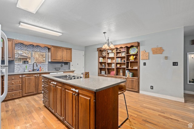 kitchen featuring a sink, black electric cooktop, brown cabinetry, a center island, and light wood-type flooring