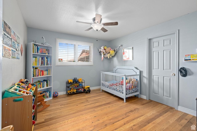 bedroom with ceiling fan, a crib, baseboards, and wood finished floors