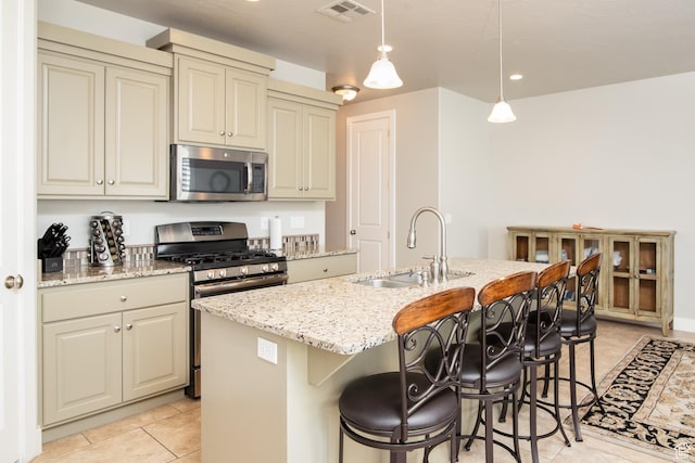 kitchen with sink, decorative light fixtures, a center island with sink, appliances with stainless steel finishes, and cream cabinetry