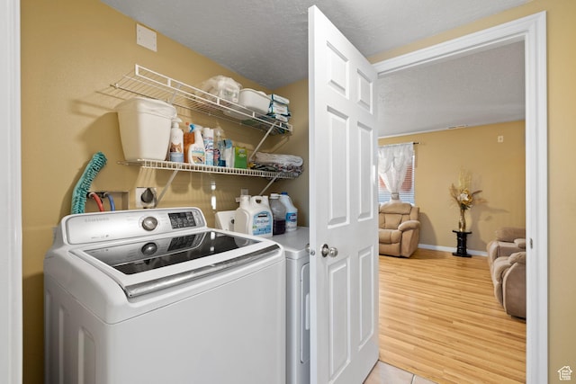 laundry area with light wood finished floors, laundry area, washing machine and dryer, baseboards, and a textured ceiling