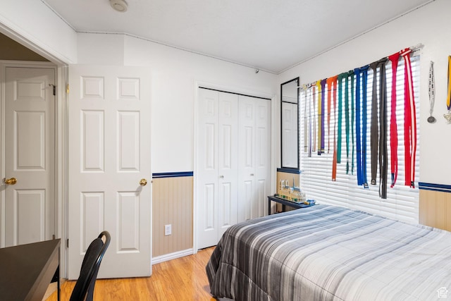 bedroom featuring light wood-style flooring, baseboards, a closet, and a wainscoted wall