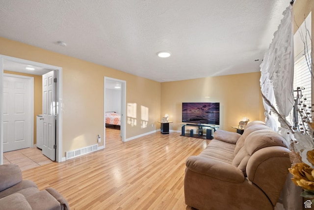 living room with light wood-type flooring, visible vents, and baseboards