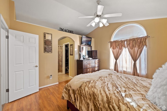 bedroom with arched walkways, vaulted ceiling, a spacious closet, wood finished floors, and ceiling fan