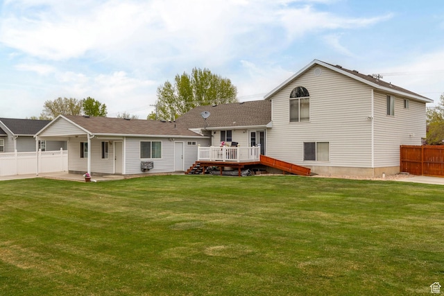 rear view of property featuring a lawn, a wooden deck, and fence