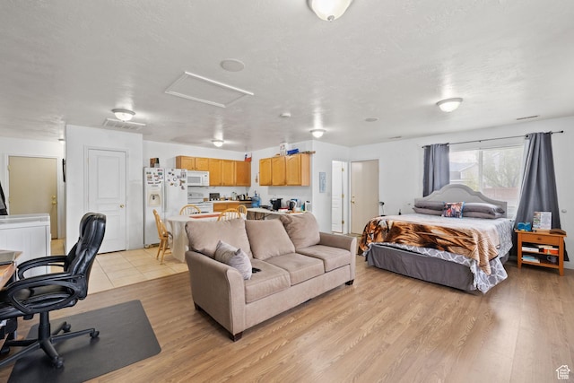 bedroom with light wood finished floors, attic access, visible vents, and white fridge with ice dispenser
