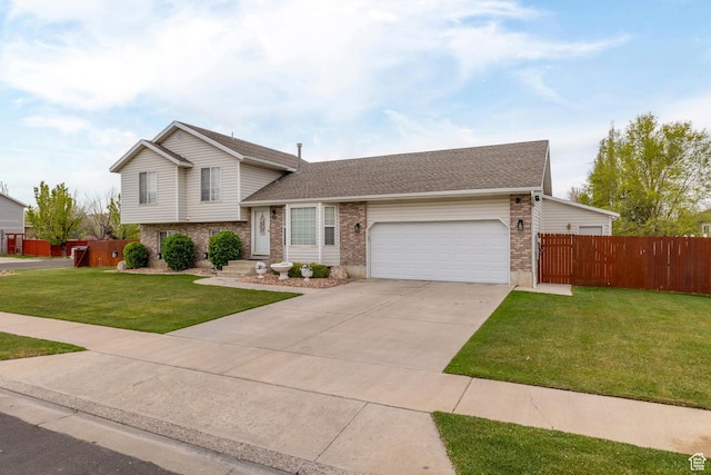 split level home featuring concrete driveway, a front lawn, fence, a garage, and brick siding