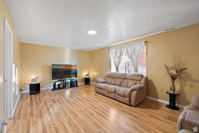 living room featuring baseboards, light wood-style floors, visible vents, and a textured ceiling