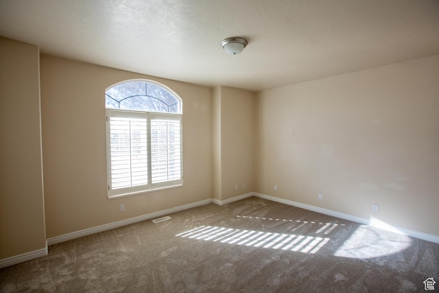 carpeted spare room featuring visible vents, baseboards, and a textured ceiling