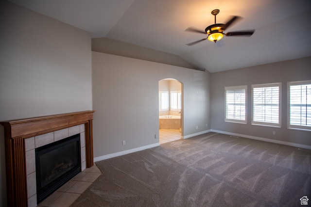 unfurnished living room featuring arched walkways, carpet, baseboards, vaulted ceiling, and a tiled fireplace