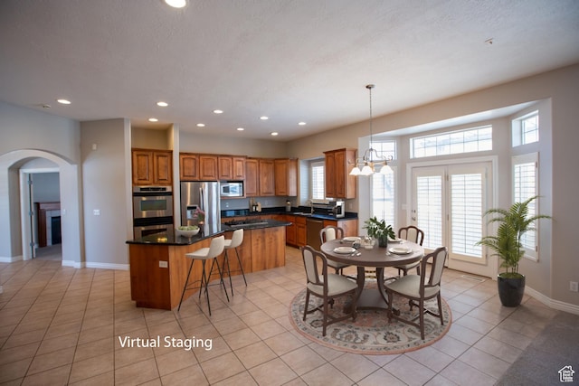 kitchen with light tile patterned flooring, stainless steel appliances, a center island, brown cabinetry, and dark countertops