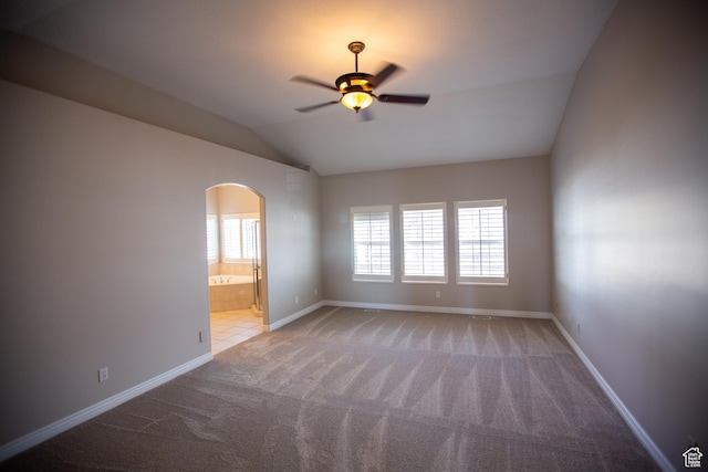 carpeted spare room featuring lofted ceiling, baseboards, arched walkways, and a ceiling fan