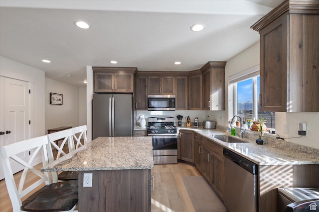 kitchen with sink, a kitchen bar, a center island, stainless steel appliances, and light stone countertops