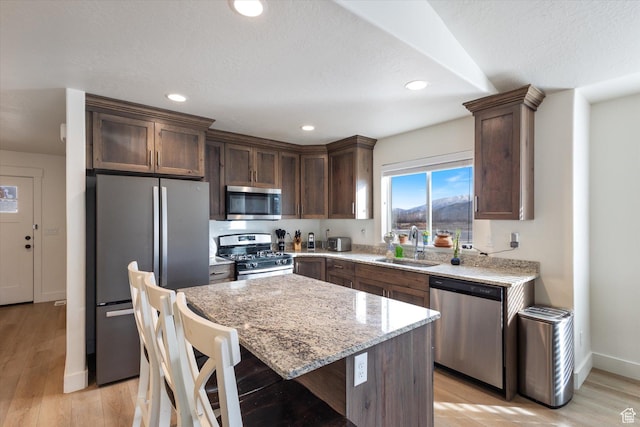 kitchen with sink, light stone counters, light hardwood / wood-style flooring, appliances with stainless steel finishes, and a kitchen island