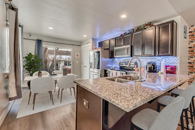 kitchen with sink, appliances with stainless steel finishes, dark brown cabinets, tasteful backsplash, and light hardwood / wood-style floors