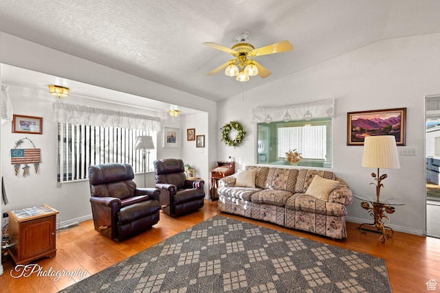 living room featuring vaulted ceiling, a textured ceiling, ceiling fan, and light wood-type flooring