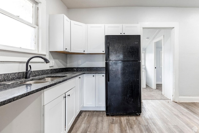 kitchen with white cabinetry, sink, dark stone counters, light hardwood / wood-style floors, and black fridge
