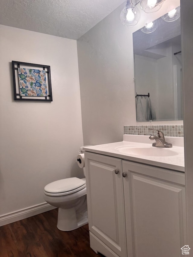 bathroom with hardwood / wood-style floors, decorative backsplash, vanity, toilet, and a textured ceiling